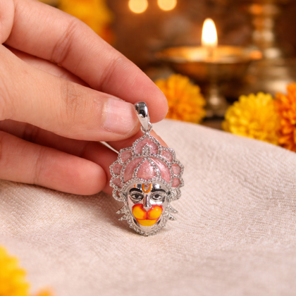 Hand holding a decorative pendant with a pink and silver design, surrounded by flowers and a lit candle.