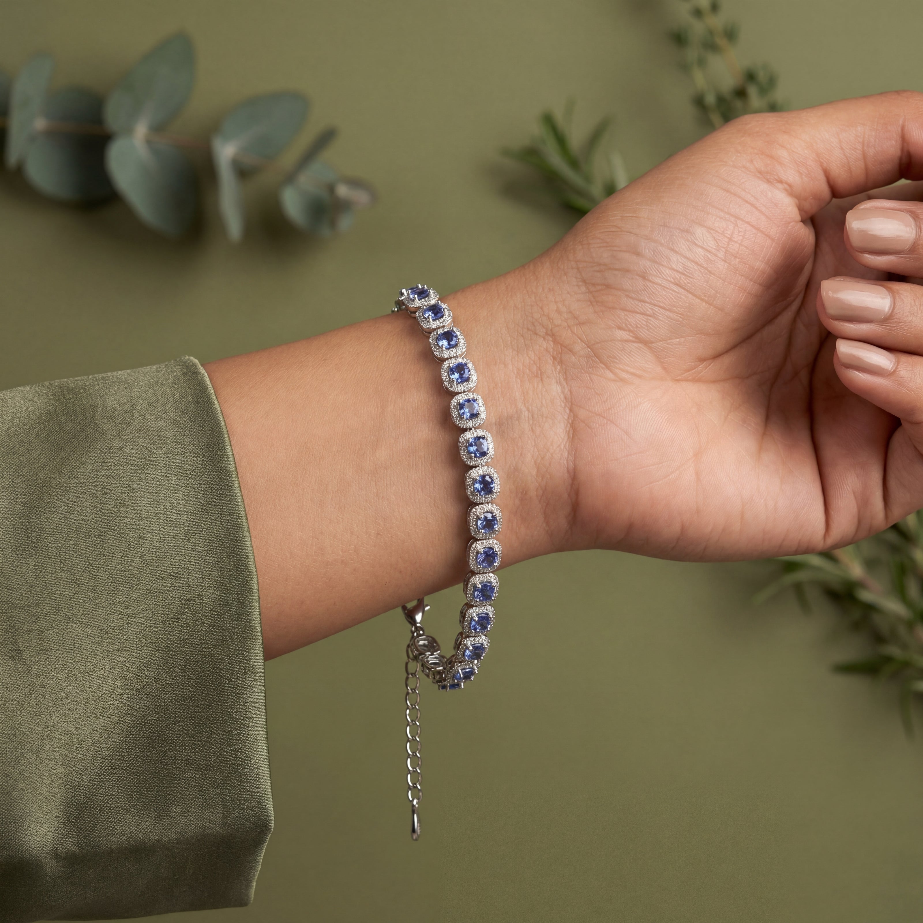 Hand wearing a bracelet with blue stones against a green background