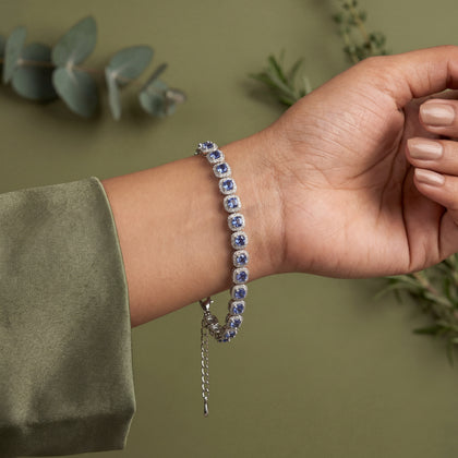 Hand wearing a bracelet with blue stones against a green background