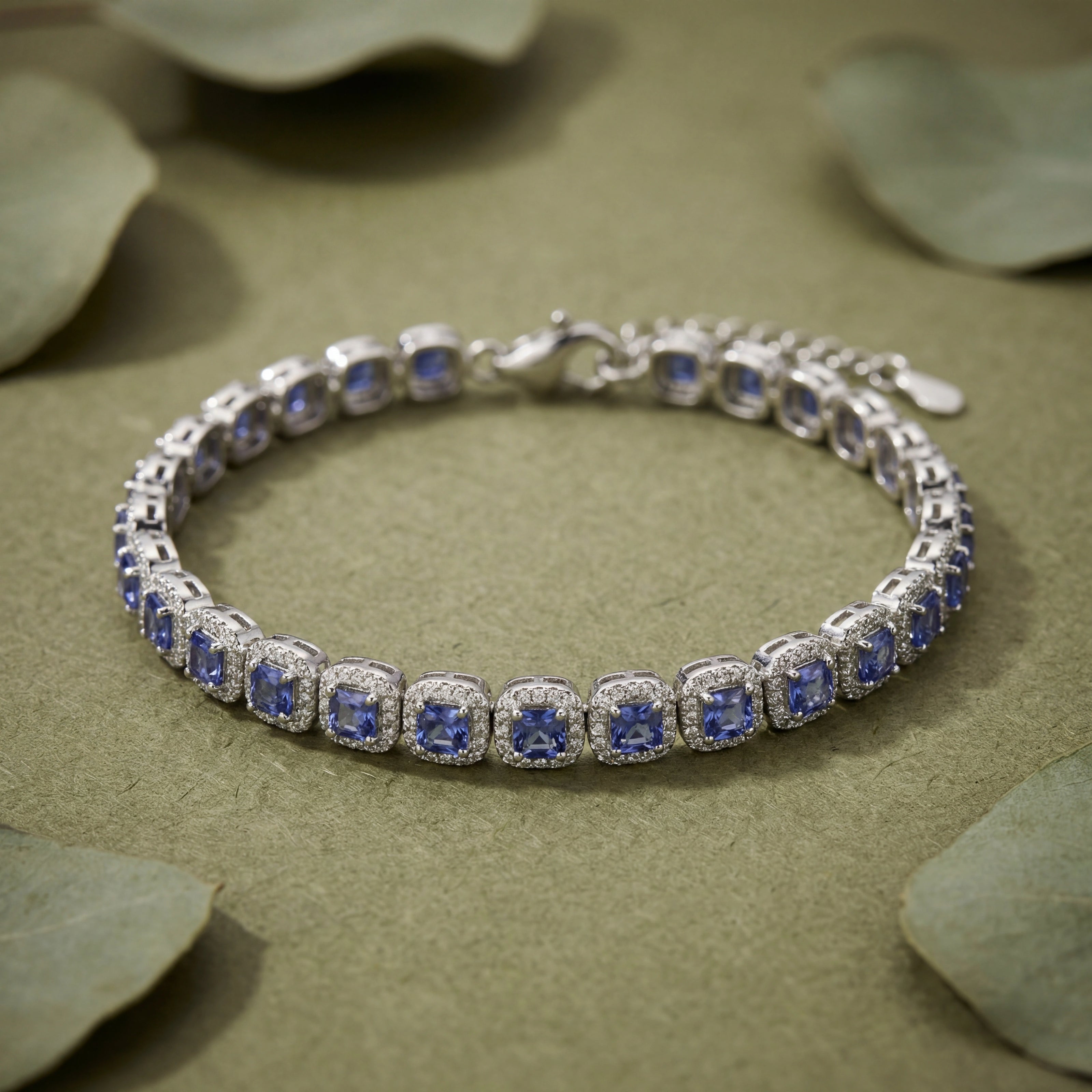 Silver bracelet with blue stones on a beige surface with green leaves