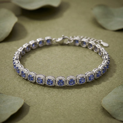 Silver bracelet with blue stones on a beige surface with green leaves