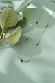 Silver necklace with a pink gemstone on a light green surface with leaves.
