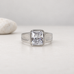 Silver ring with a large rectangular clear stone and engraved geometric band.