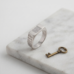 Silver ring with a rectangular stone-studded face and square lattice cutout band.