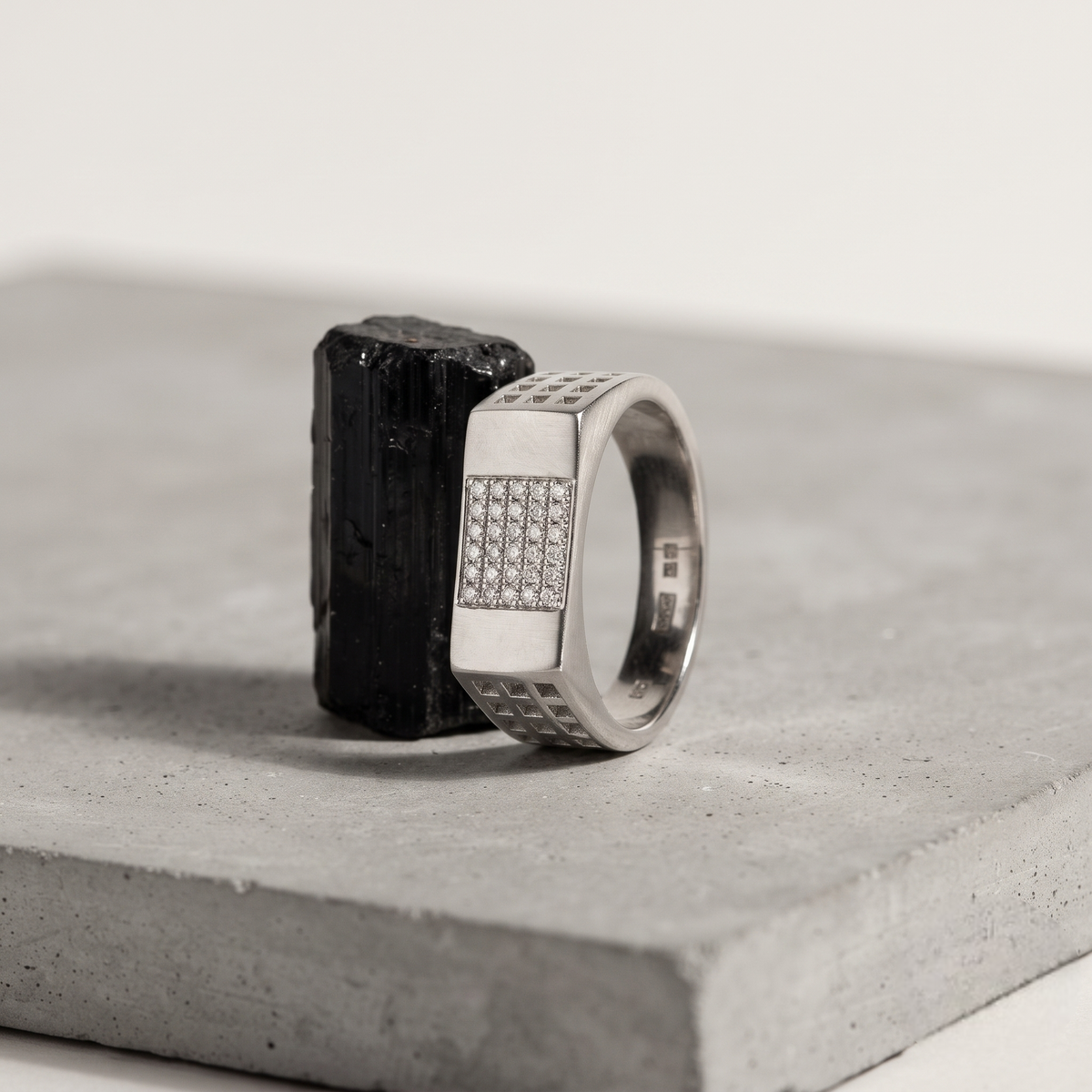 Silver ring with a rectangular stone-studded face and square lattice cutout band.