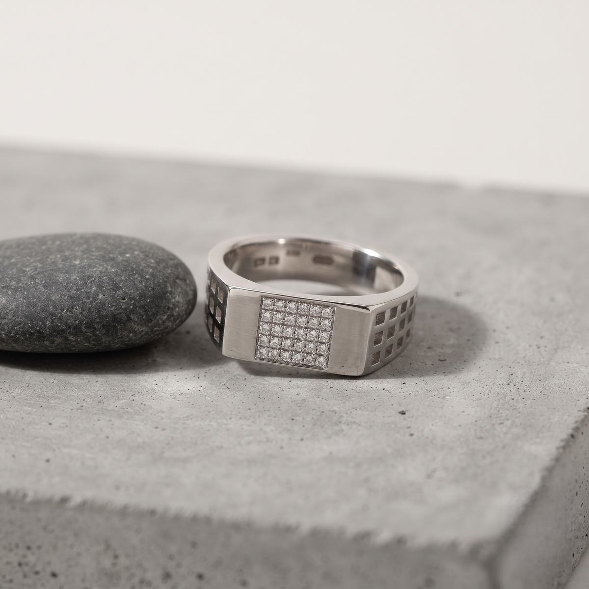 Silver ring with a rectangular stone-studded face and square lattice cutout band.