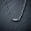 Silver paperclip chain with an oval stone-studded centrepiece.