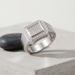 Silver ring with a square pavé-set centre, stone-studded halo and wide polished band.