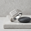 Silver ring with a square pavé-set centre, stone-studded halo and wide polished band.