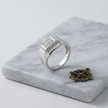 Silver ring with a square pavé-set centre, stone-studded halo and wide polished band.