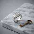 Silver ring with a square pavé-set centre, stone-studded halo and wide polished band.