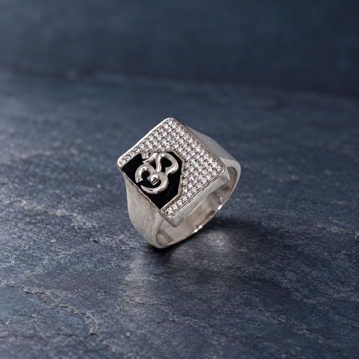 Silver ring with an Om symbol on a black centre and square stone-studded border.