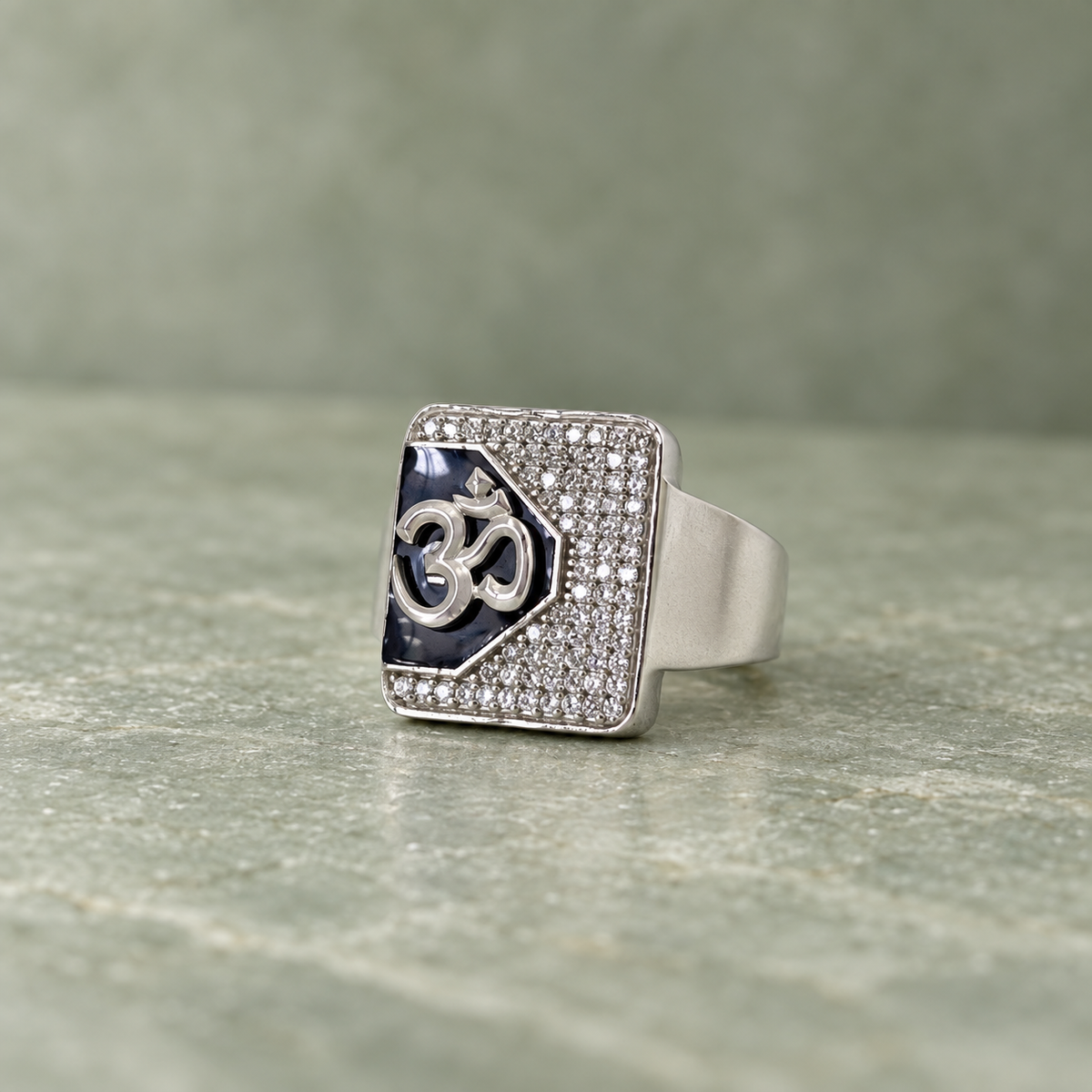 Silver ring with an Om symbol on a black centre and square stone-studded border.