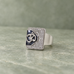Silver ring with an Om symbol on a black centre and square stone-studded border.