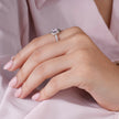 Pink cubic zirconia halo ring in 925 sterling silver displayed on a sandy beach with ocean waves and seashells, showcasing elegant women's jewelry in a coastal setting.