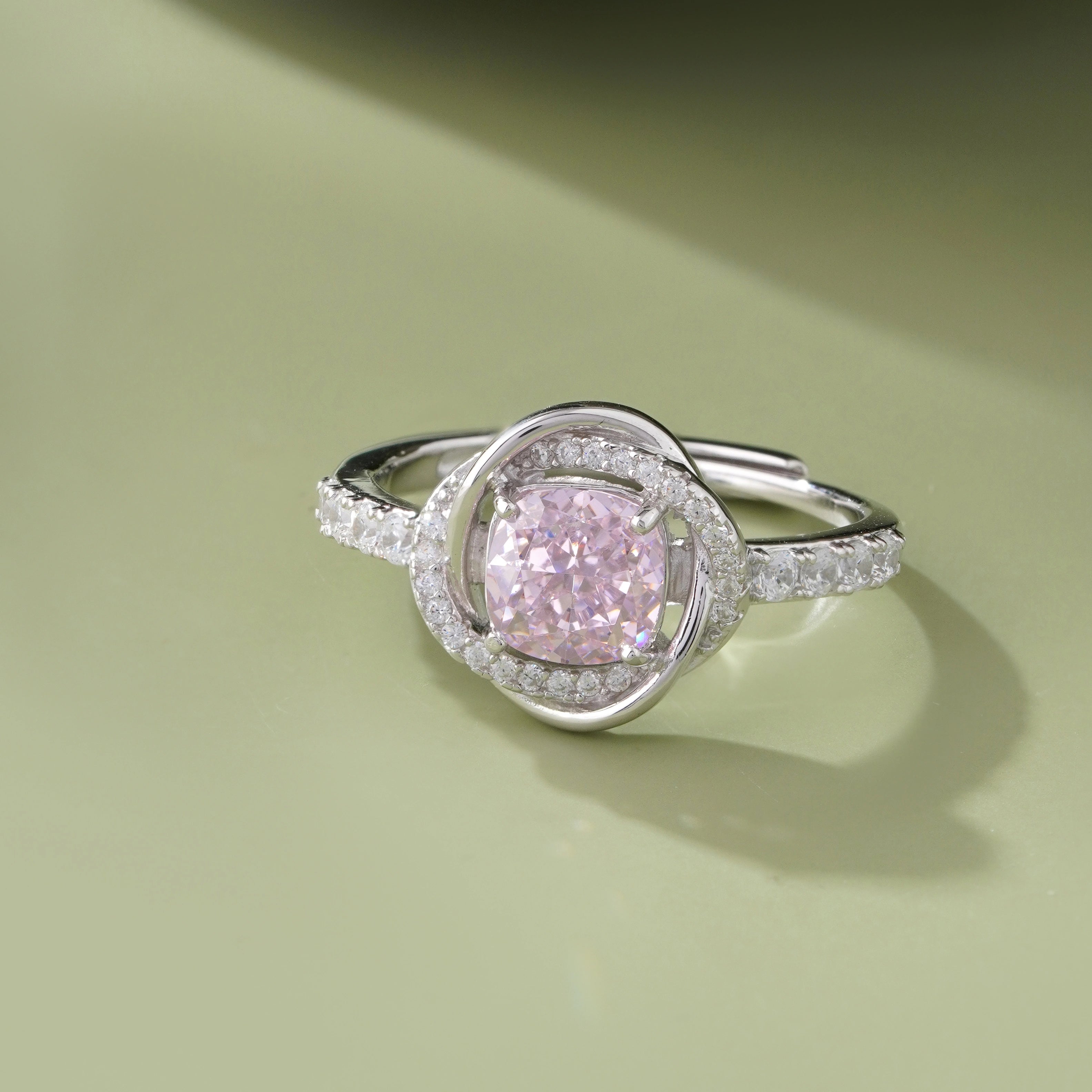 Pink cubic zirconia halo ring in 925 sterling silver displayed on a sandy beach with ocean waves and seashells, showcasing elegant women's jewelry in a coastal setting.