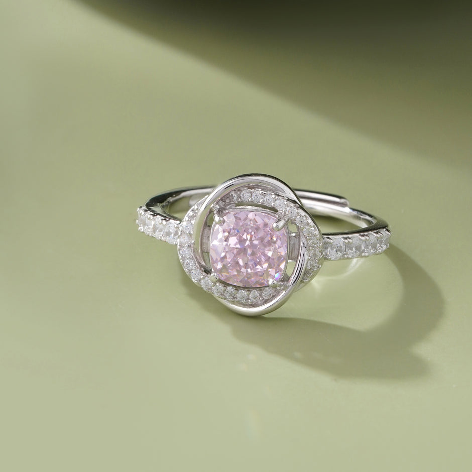 Pink cubic zirconia halo ring in 925 sterling silver displayed on a sandy beach with ocean waves and seashells, showcasing elegant women's jewelry in a coastal setting.