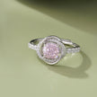 Pink cubic zirconia halo ring in 925 sterling silver displayed on a sandy beach with ocean waves and seashells, showcasing elegant women's jewelry in a coastal setting.