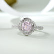 Pink cubic zirconia halo ring in 925 sterling silver displayed on a sandy beach with ocean waves and seashells, showcasing elegant women's jewelry in a coastal setting.