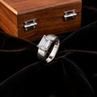 Silver ring with an emerald-cut clear solitaire stone and wide polished band.