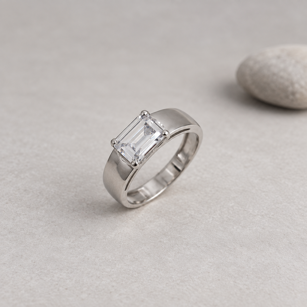 Silver ring with an emerald-cut clear solitaire stone and wide polished band.