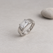 Silver ring with an emerald-cut clear solitaire stone and wide polished band.