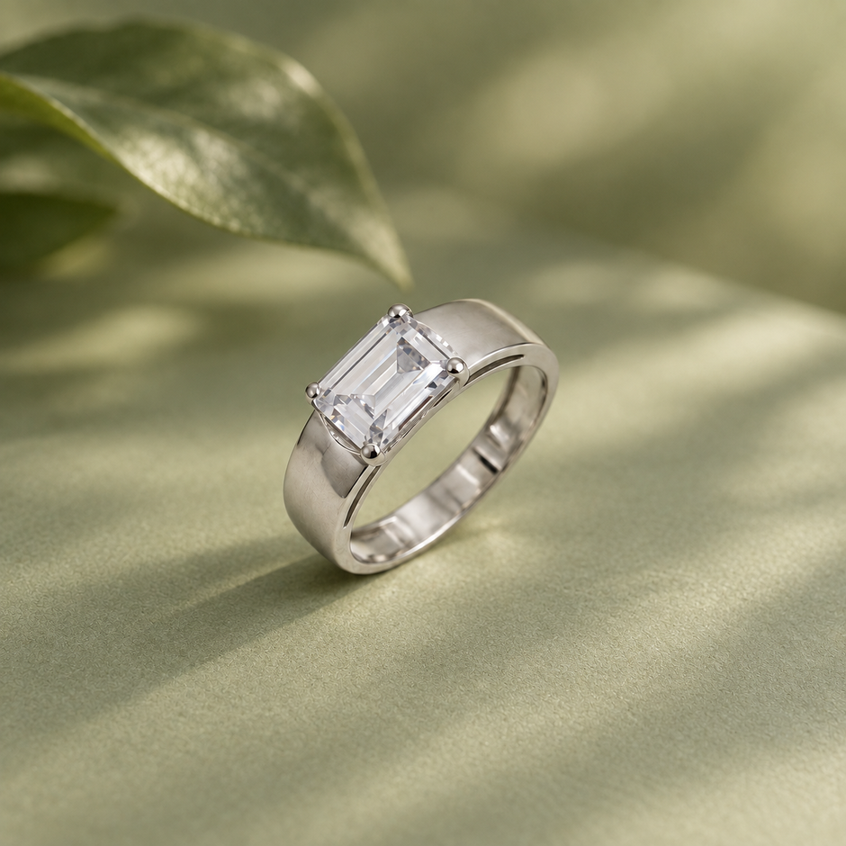 Silver ring with an emerald-cut clear solitaire stone and wide polished band.
