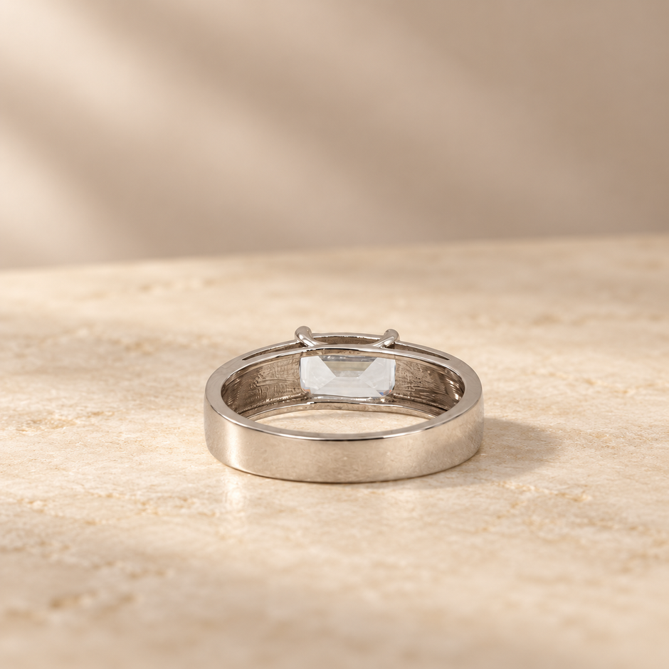 Silver ring with an emerald-cut clear solitaire stone and wide polished band.