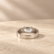 Silver ring with an emerald-cut clear solitaire stone and wide polished band.