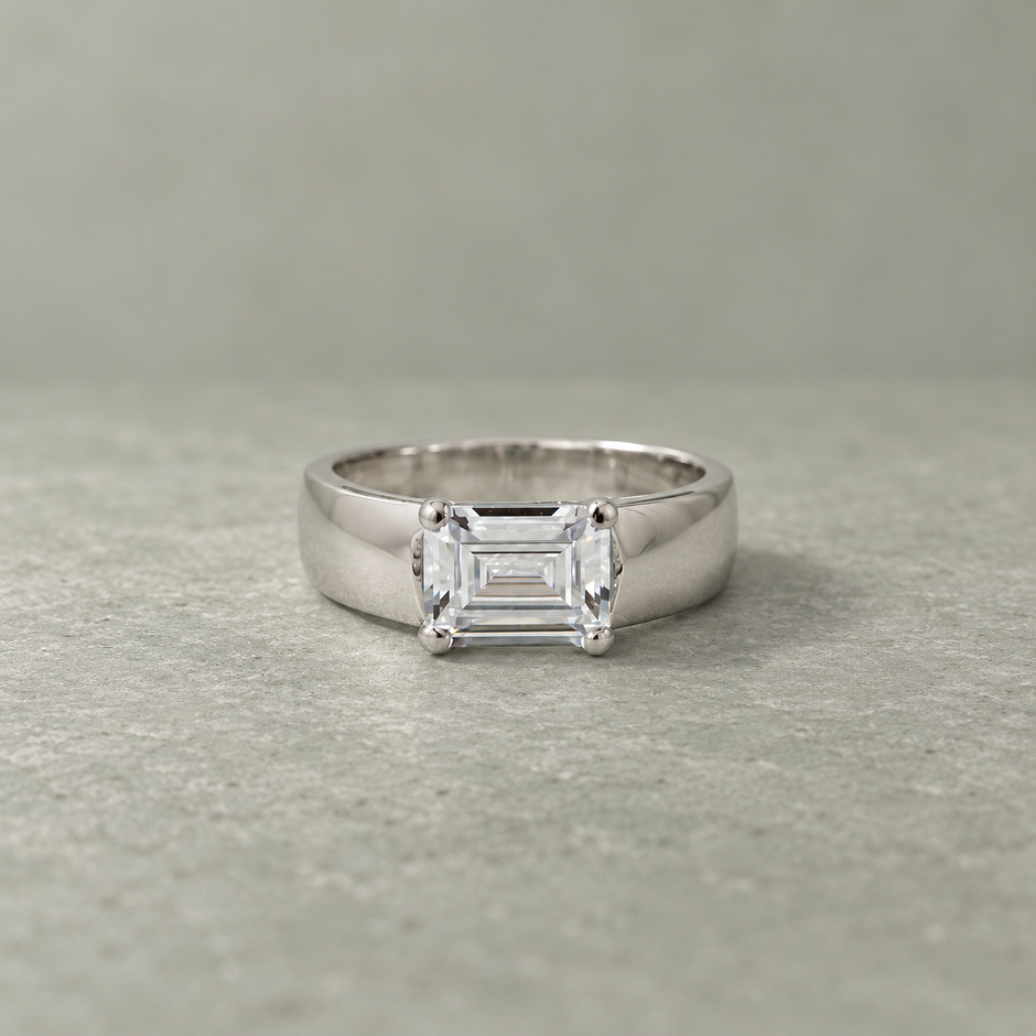 Silver ring with an emerald-cut clear solitaire stone and wide polished band.