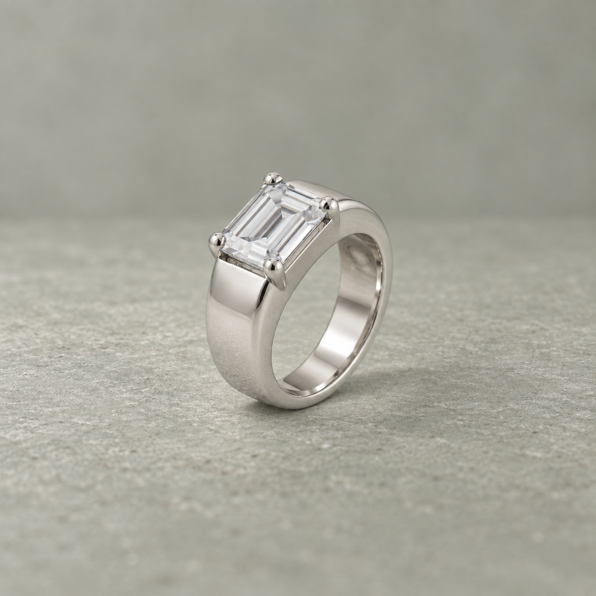 Silver ring with an emerald-cut clear solitaire stone and wide polished band.