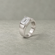 Silver ring with an emerald-cut clear solitaire stone and wide polished band.