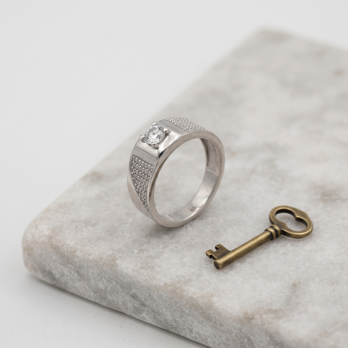 Silver ring with a round clear centre stone, square setting and pavé-set shoulders.