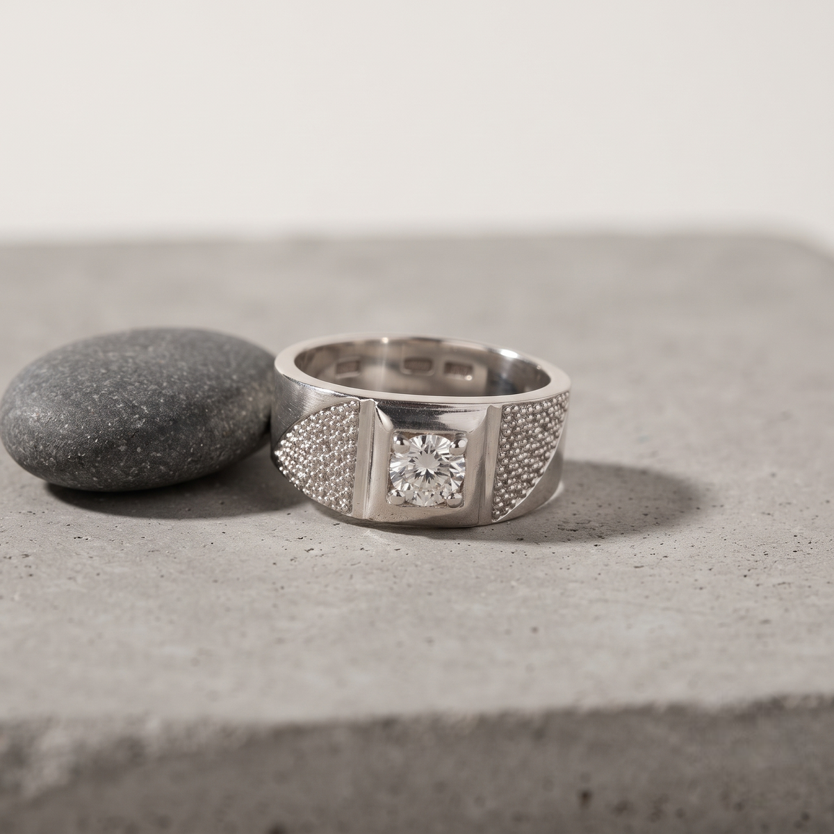 Silver ring with a round clear centre stone, square setting and pavé-set shoulders.