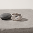 Silver ring with a round clear centre stone, square setting and pavé-set shoulders.