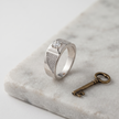 Silver ring with a round clear centre stone, square setting and pavé-set shoulders.