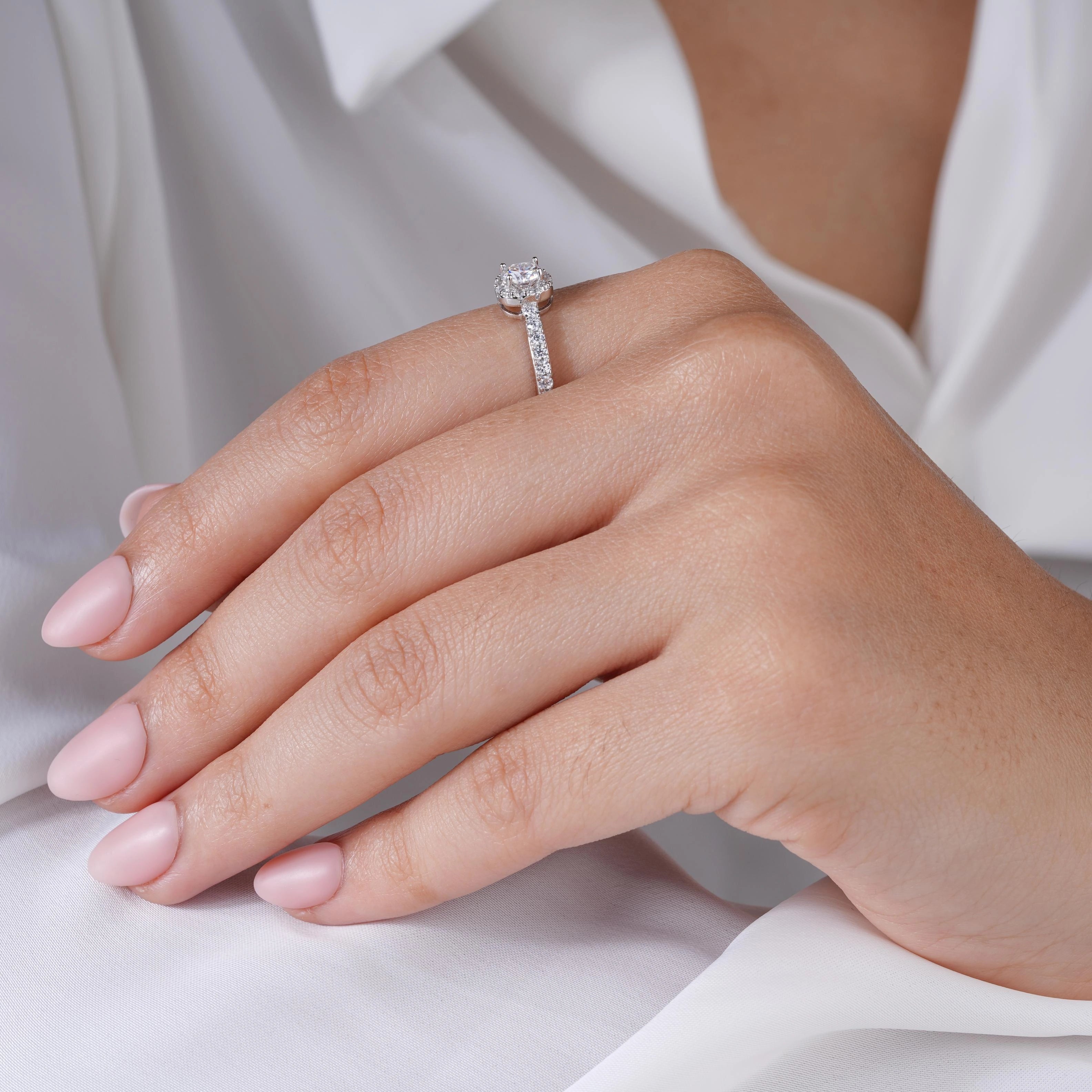 925 sterling silver halo engagement ring with a round brilliant-cut center stone and pavé band, worn on a woman's hand against a soft white background.