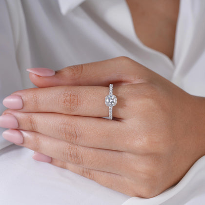 925 sterling silver halo engagement ring with a round brilliant-cut center stone and pavé band, worn on a woman's hand against a soft white background.