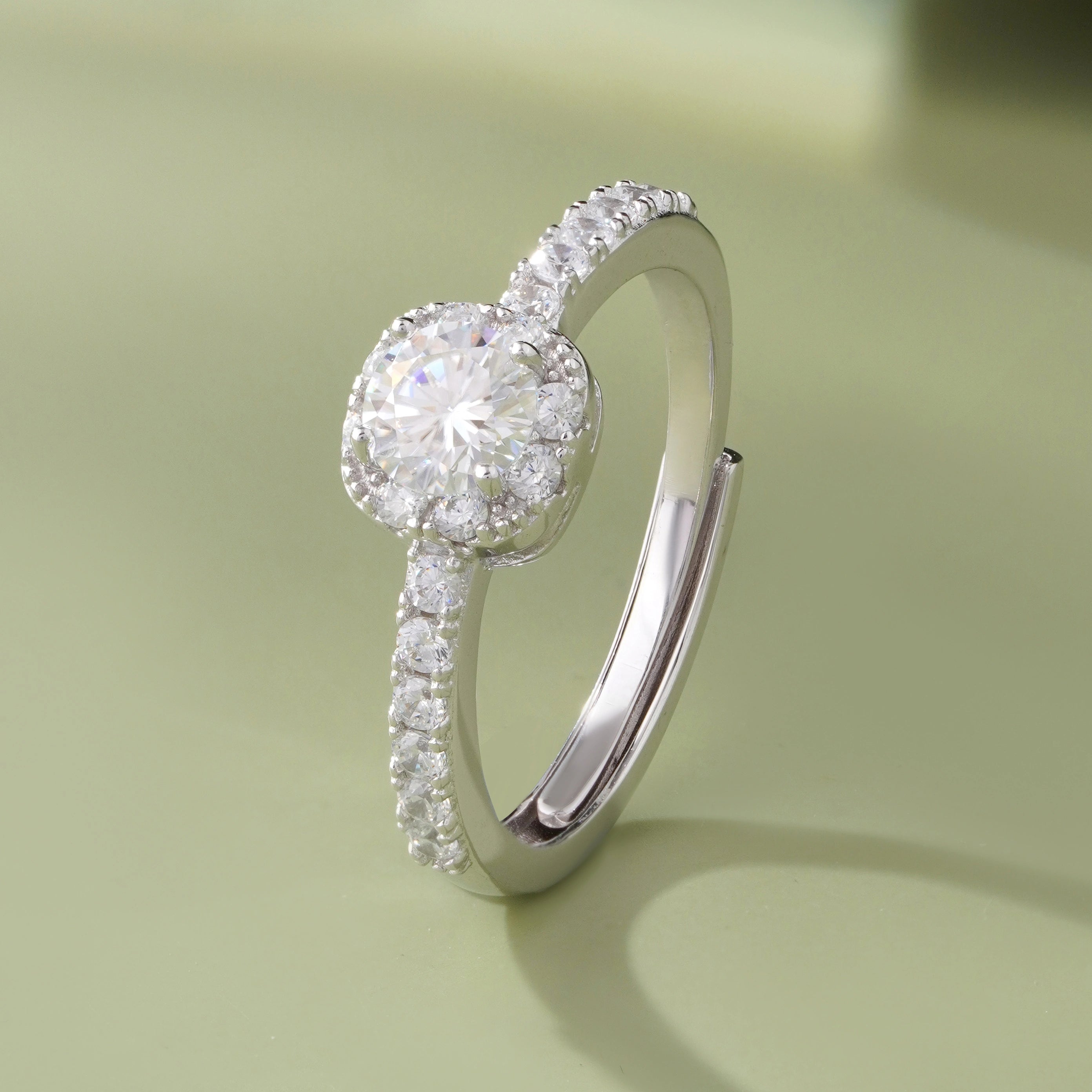 925 sterling silver halo engagement ring with a round brilliant-cut center stone and pavé band, worn on a woman's hand against a soft white background.
