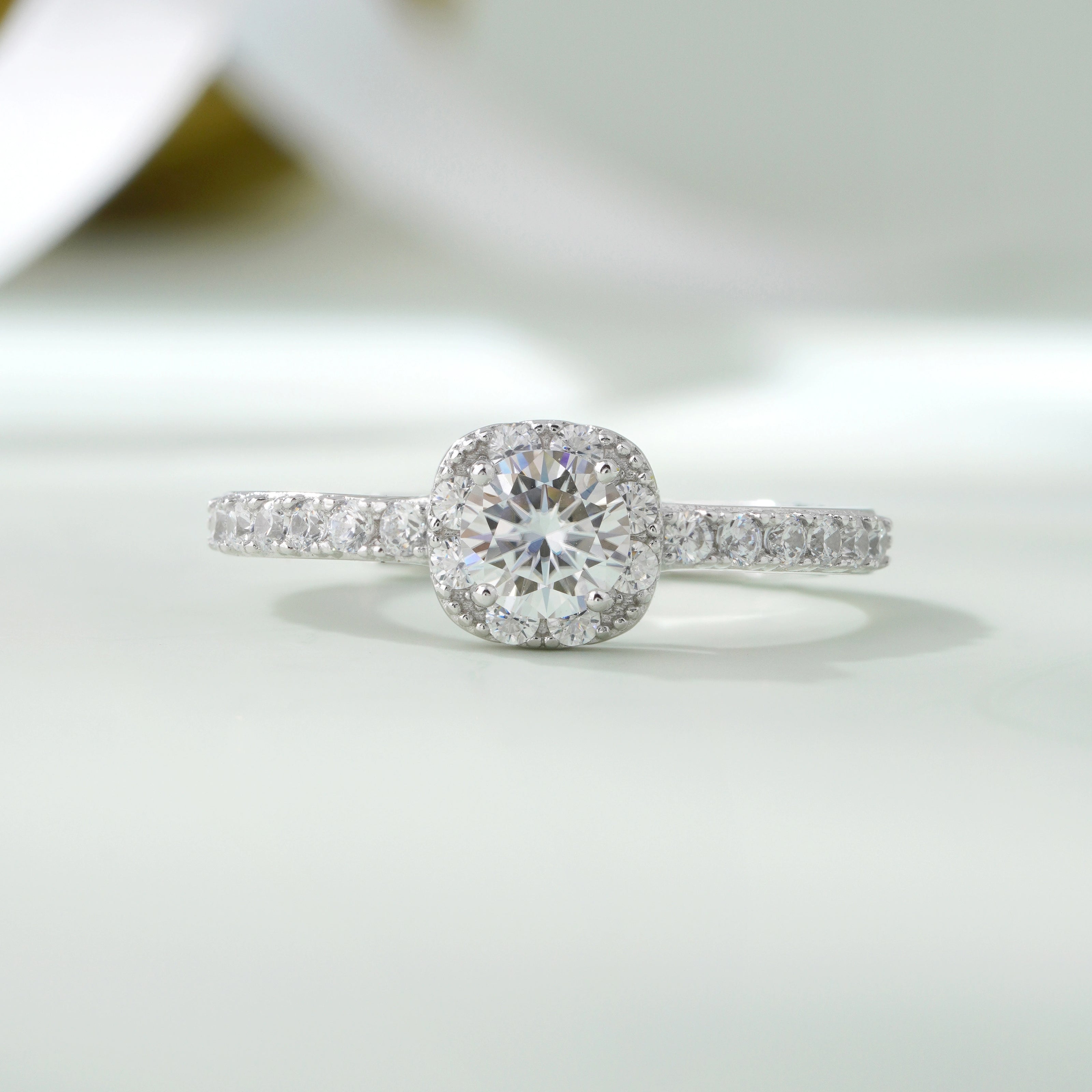 925 sterling silver halo engagement ring with a round brilliant-cut center stone and pavé band, worn on a woman's hand against a soft white background.
