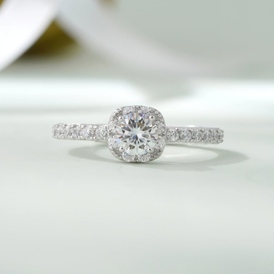925 sterling silver halo engagement ring with a round brilliant-cut center stone and pavé band, worn on a woman's hand against a soft white background.