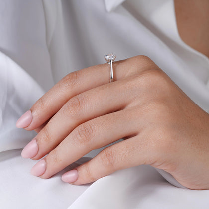 925 sterling silver solitaire ring with a round brilliant-cut stone, worn on a woman's hand against a soft white fabric background.