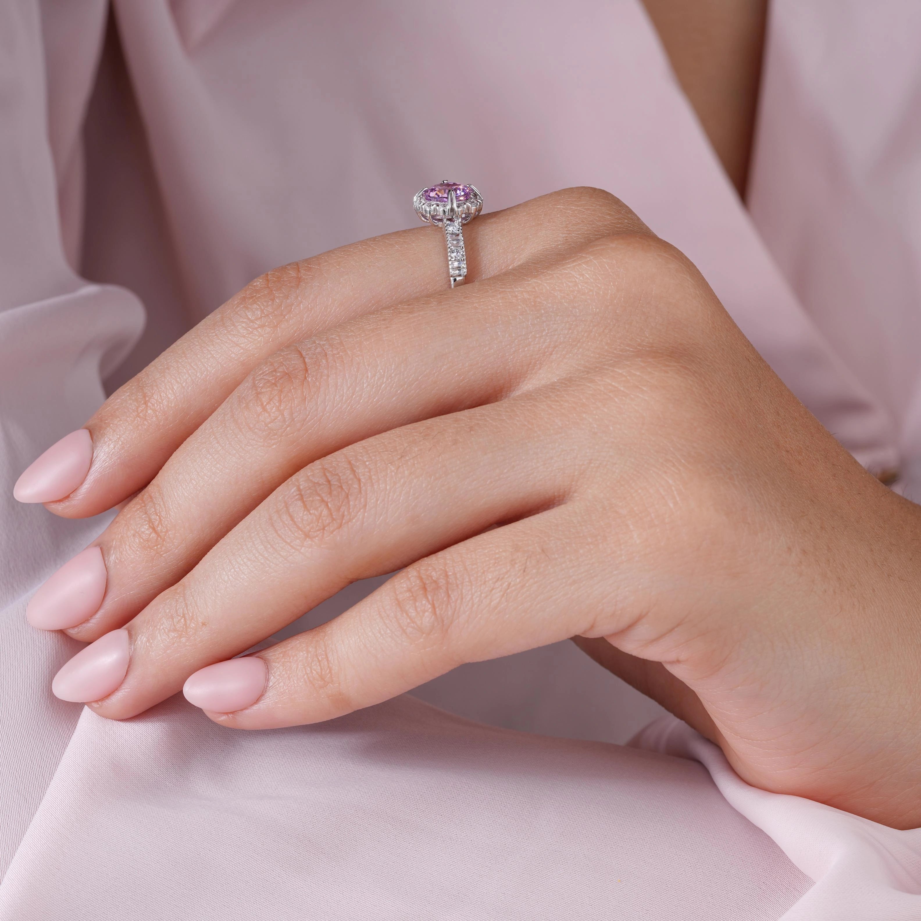 Close-up of a hand wearing a ring with a pink gemstone on a soft pink fabric background