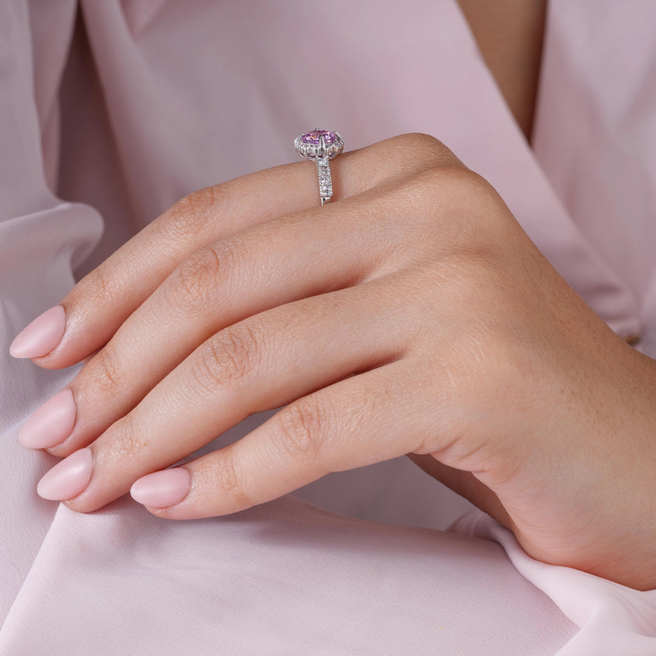 Close-up of a hand wearing a ring with a pink gemstone on a soft pink fabric background