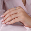 Close-up of a hand wearing a ring with a pink gemstone on a soft pink fabric background