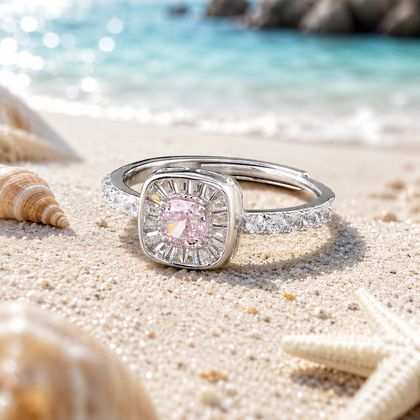 925 sterling silver halo ring with a pink cushion-cut center stone and sparkling cubic zirconia accents, displayed on sandy beach background with ocean waves.